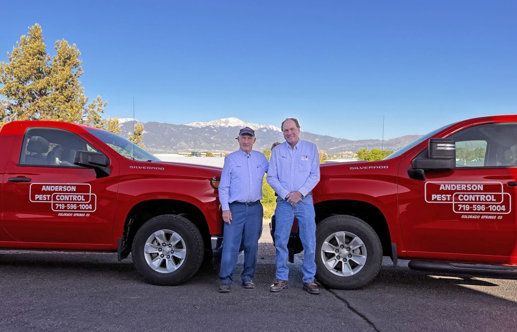 two men standing in front of red Anderson Pest Control trucks