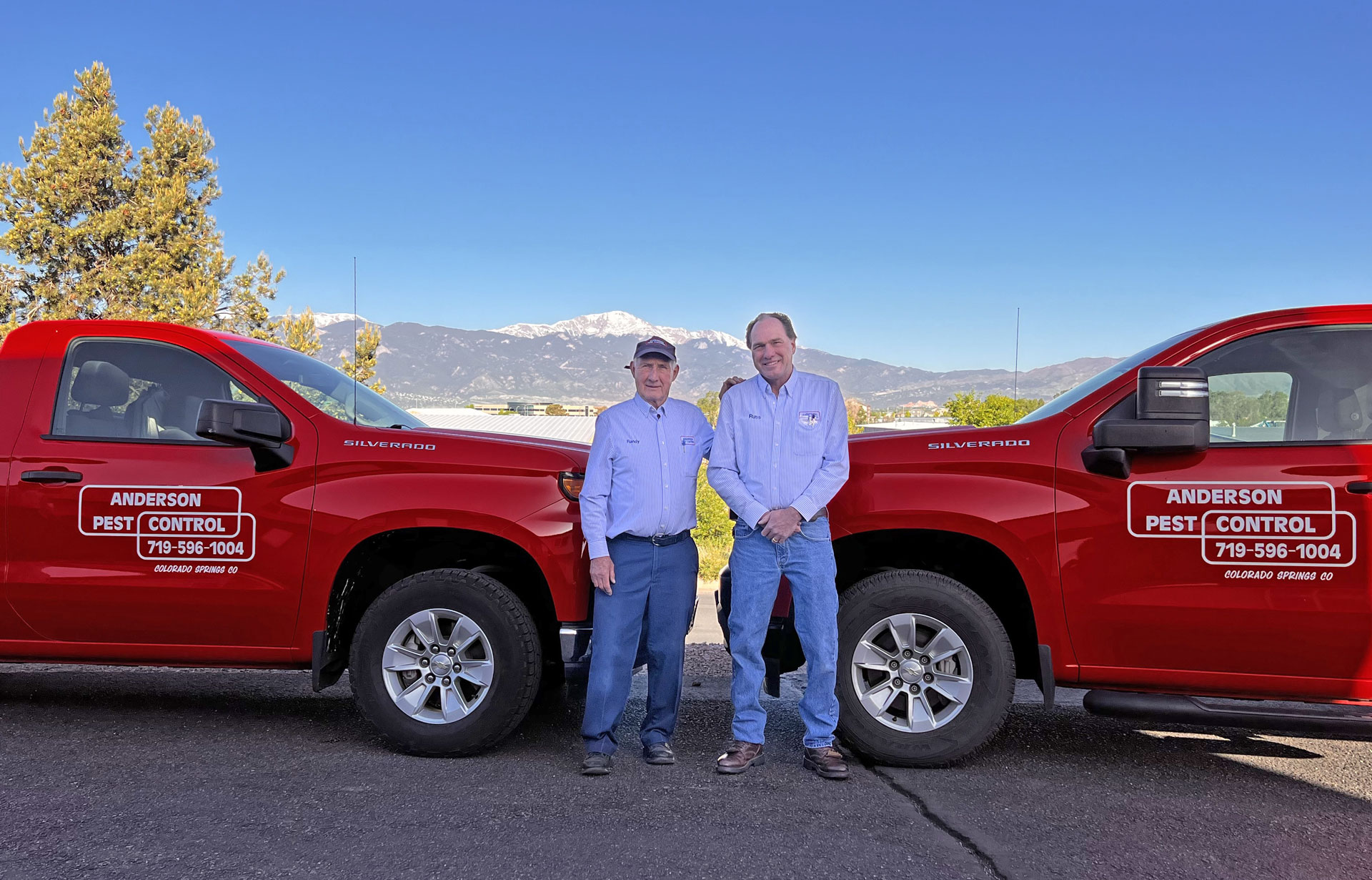 two men standing in front of red Anderson Pest Control trucks